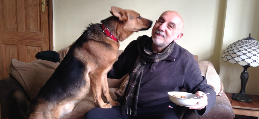 Armen sitting on a sofa with a dog sat next to him, holding its nose close to Armen's face