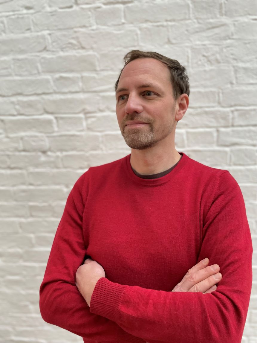 A profile photo of Dr Malte Gerhold, showing a person in a red jumper stood in front of a white wall