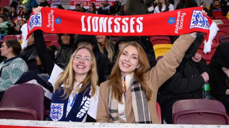Two football fans with a Lionesses scarf that has the Alzheimer's Society logo on 