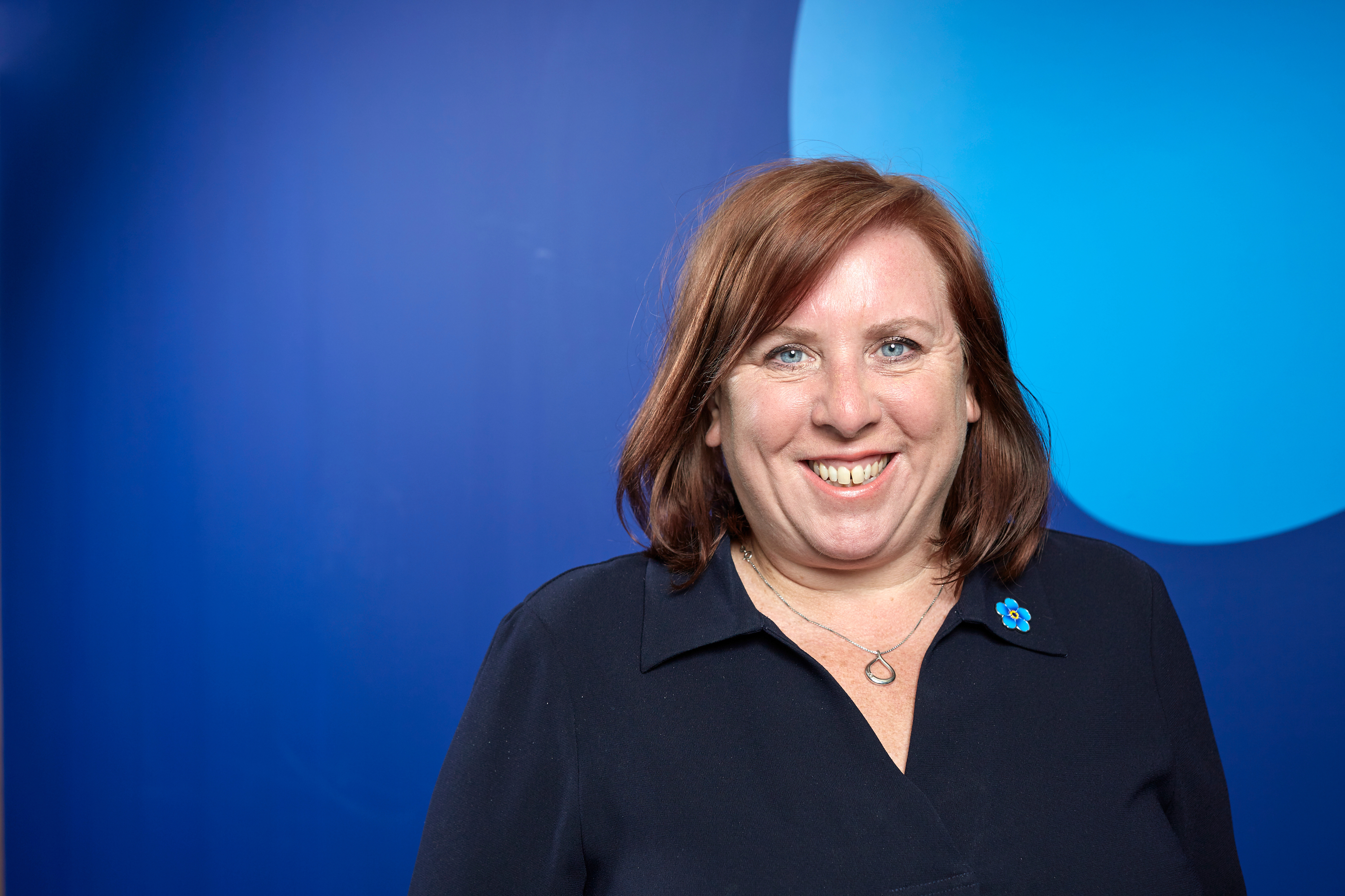 Photo of Alzheimer's Society Chief Policy and Research Officer Fiona Carragher. Fiona is smiling and wearing an Alzheimer's Society Forget Me Not flower brooch