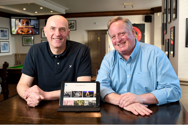 An image of the two founders of Memory Lane Games, sat at a table with a tablet in front of them, showcasing the product. They are both smiling. 