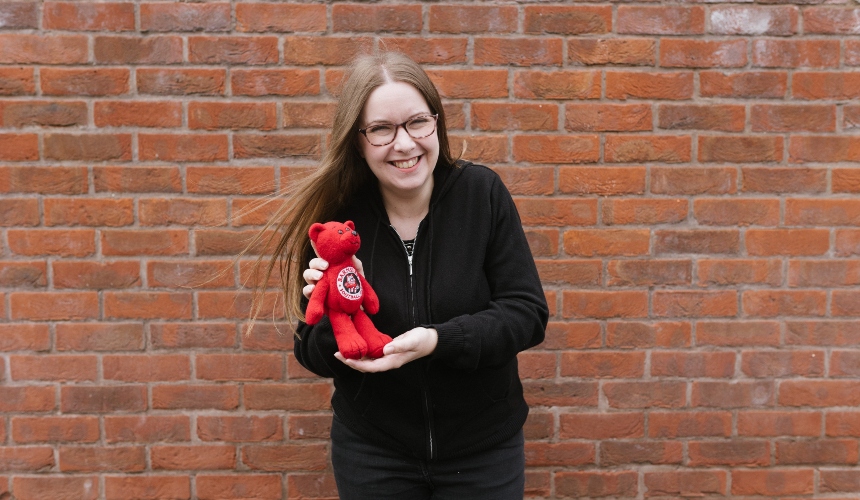 Jenny stands in front of a wall, holding her Barnsley branded teddy bear and laughing