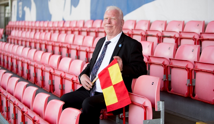 Peter Jones sits in a football stand, holding a flag