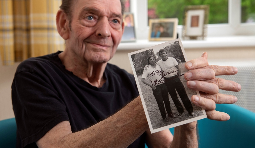 Stan, who has dementia, holds up a signed photograph of himself and Mike Summerbee