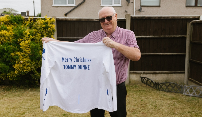 Tommy holds up a white shirt that has 'Merry Christmas Tommy Dunne' written on it