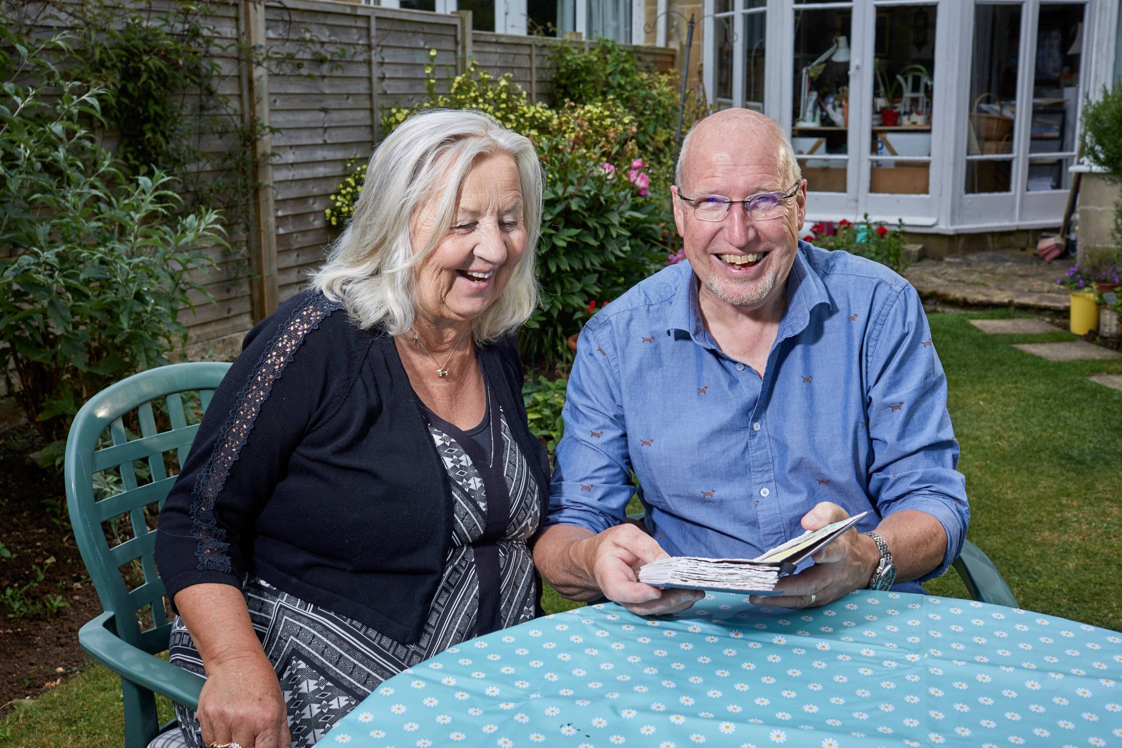 Two people, a man and a woman, are sitting side by side, smiling  as they look at a book together.