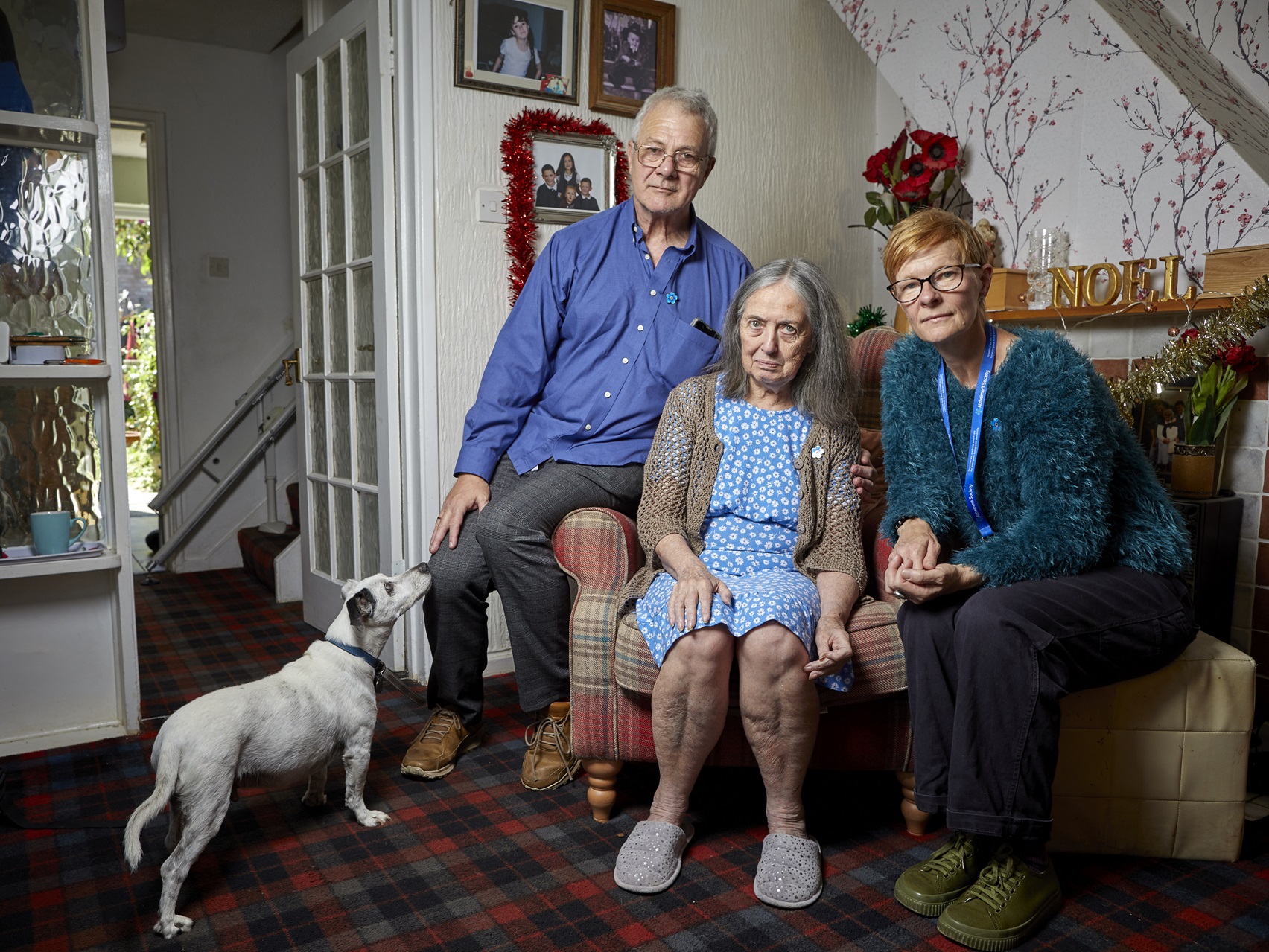 A person with dementia and her husband are sitting together on a sofa chair, alongside their dementia advisor.