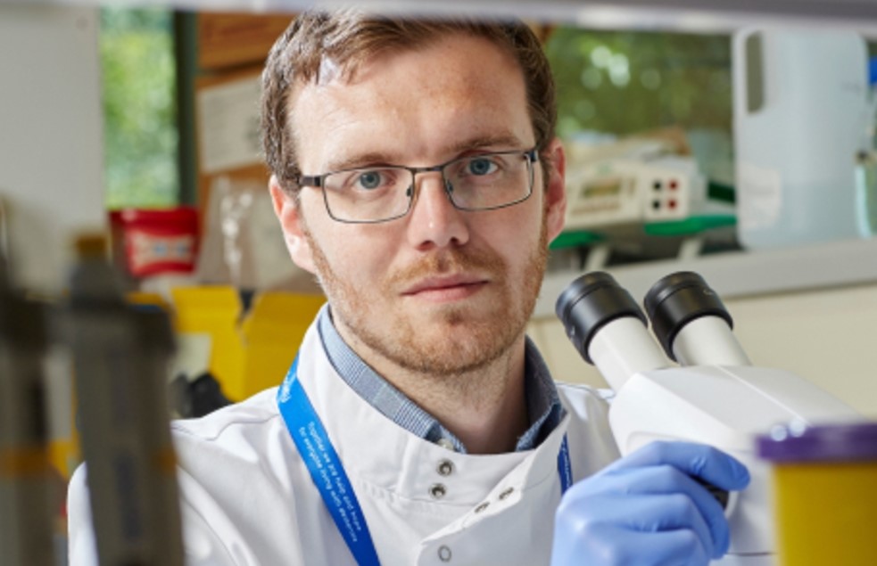 A man in a white lab coat looks up from his microscope