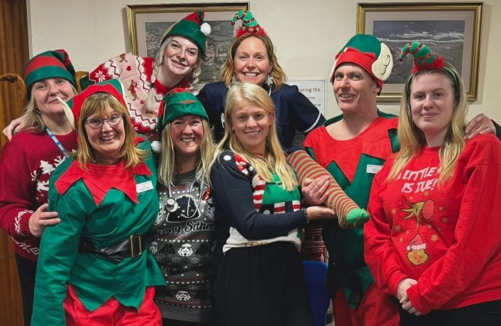 A group of men and women in elf costumes squeeze together for a photo.