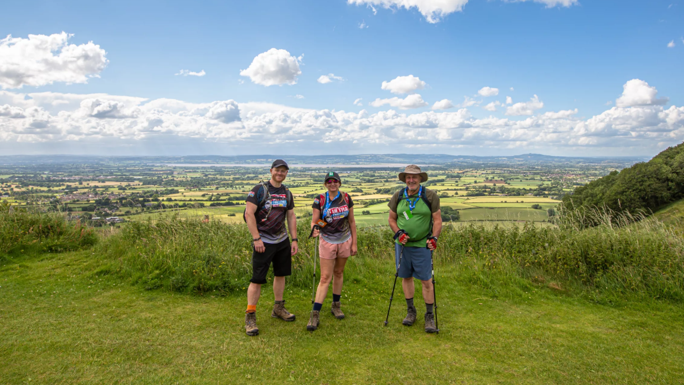 Three trekkers stand atop a hill with a country vista in the background