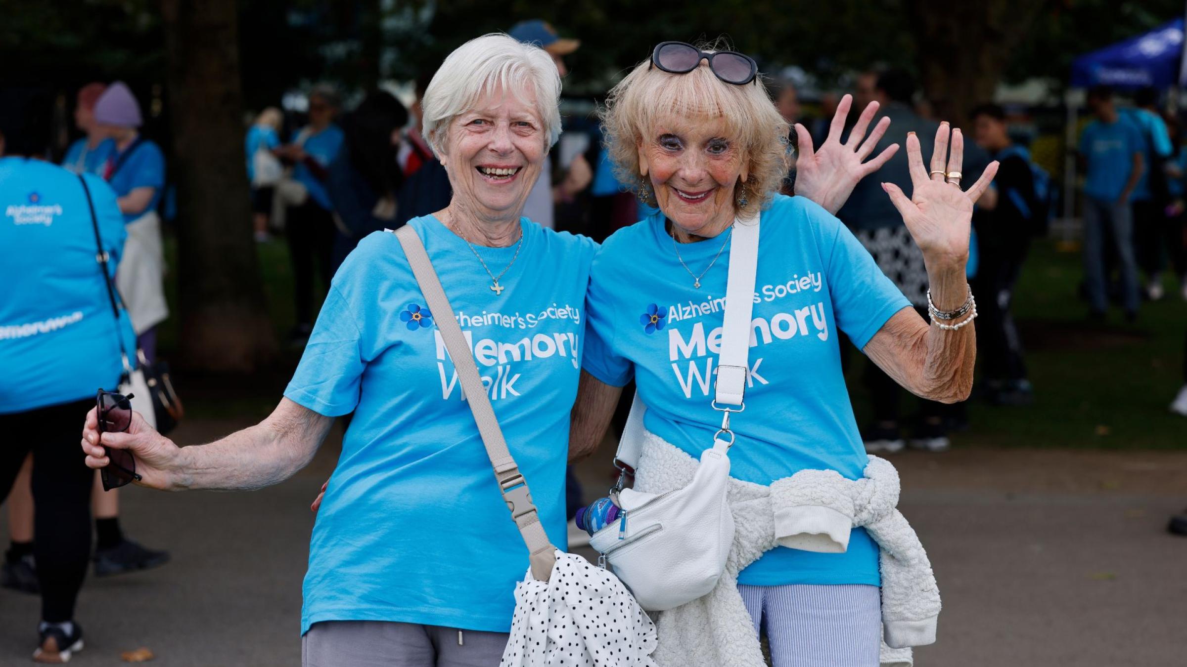 Two women in blue t-shits smiling and waving 