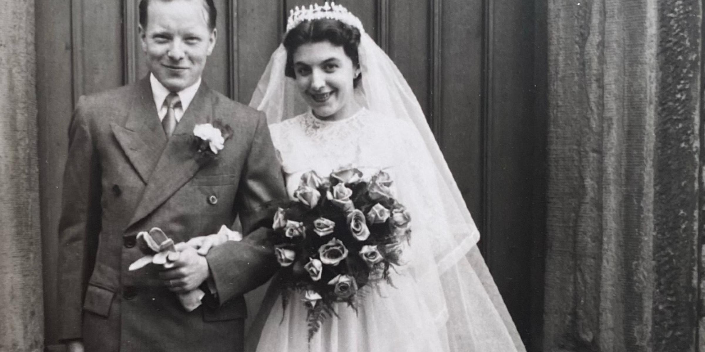 A black and white photo of Barbara and Peter standing together arms linked in their wedding clothes