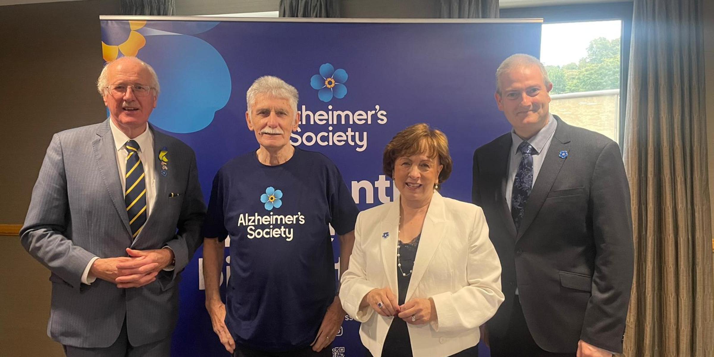 Three men and a lady stood in front of Alzheimer's Society branding