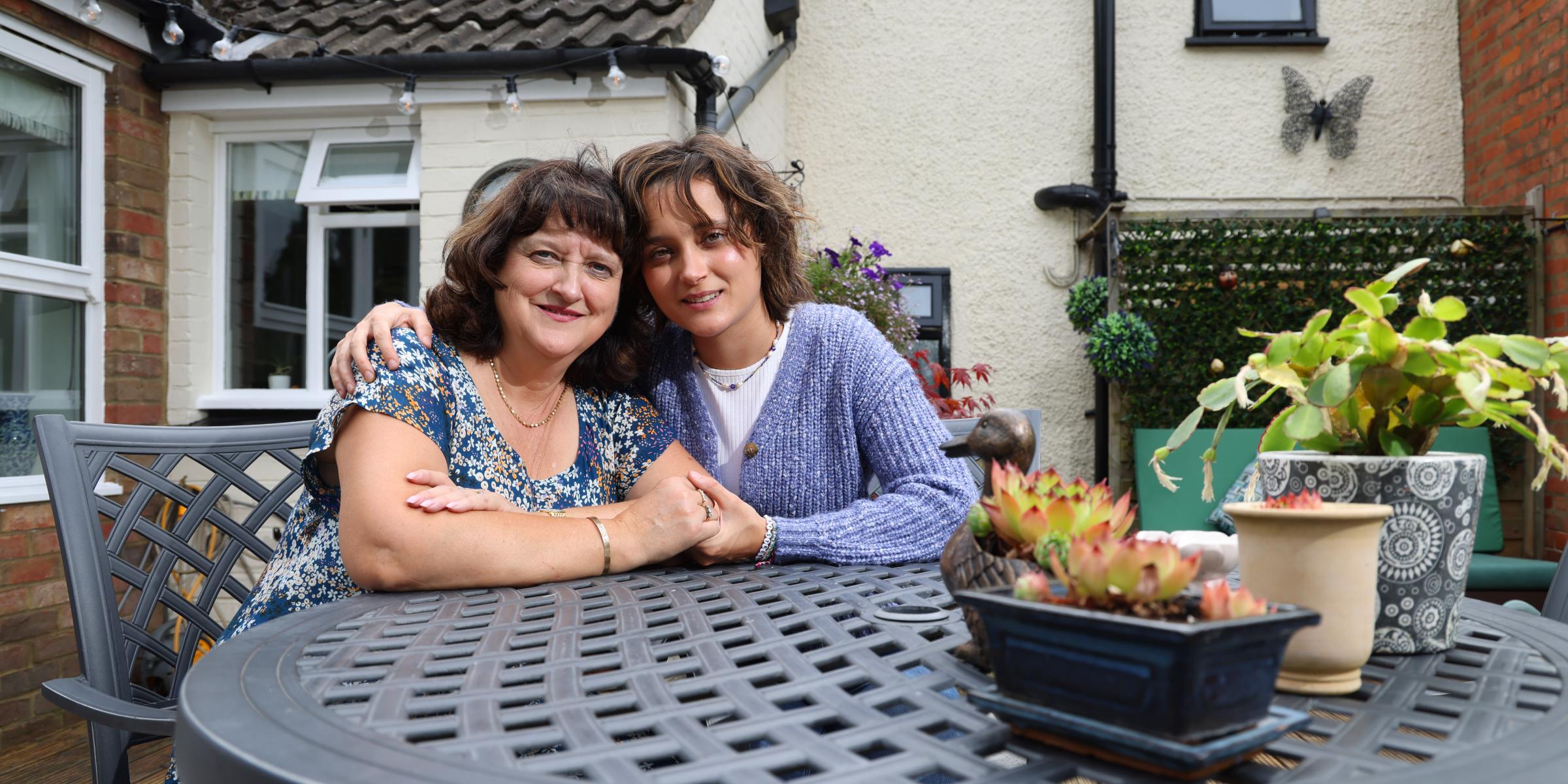 Jane and her child sit at a garden table with their arms around each other