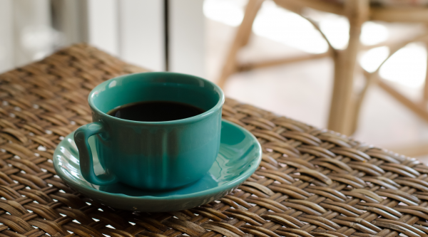 A green coffee mug on a brown wicker table