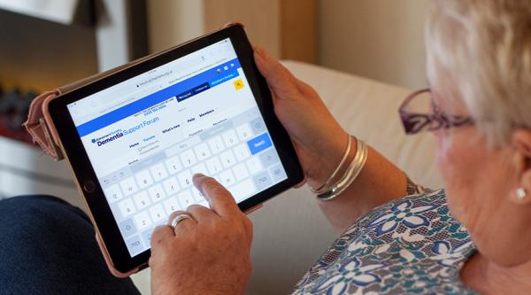 Woman with grey hair and glasses using a tablet to search the Dementia Support Forum