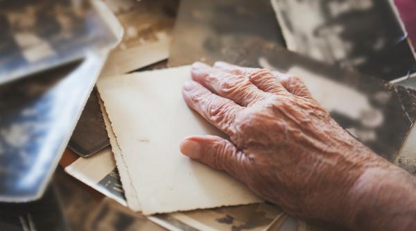 An older person's hand on top of some photographs, which are face down.