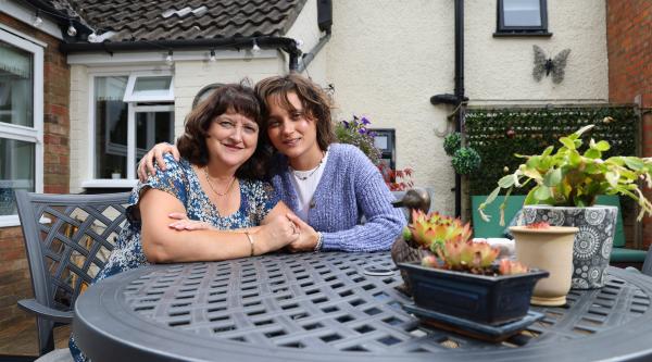 Jane and her child sit at a garden table with their arms around each other 