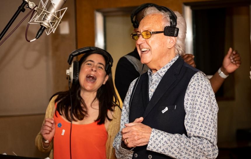 Tony Christie and Zoe Antoniades in a recording studio singing into a microphone