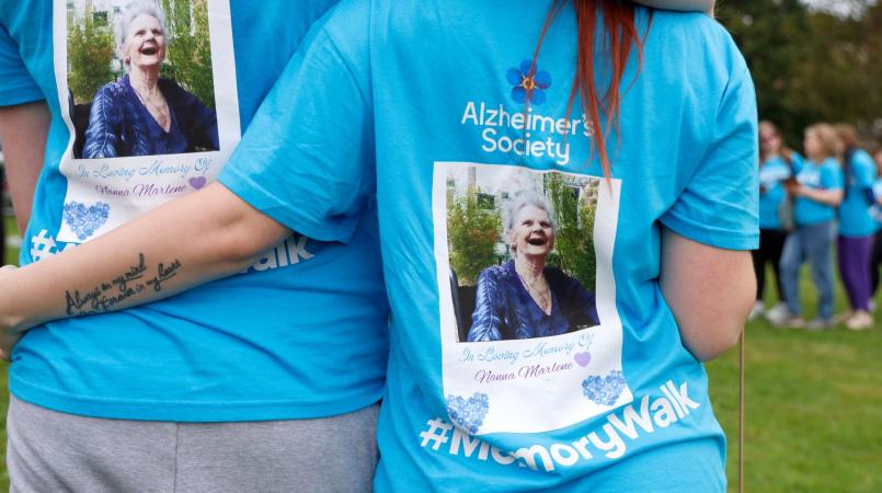 2 people arm in arm with their backs to the camera, wearing blue Memory Walk t-shirts with images of a loved one on the back.