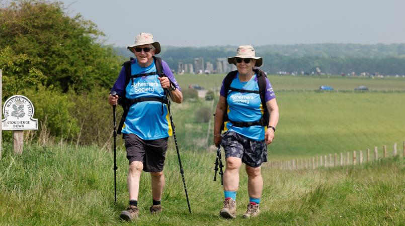 Two people trekking up hill in front of Stonehenge monument