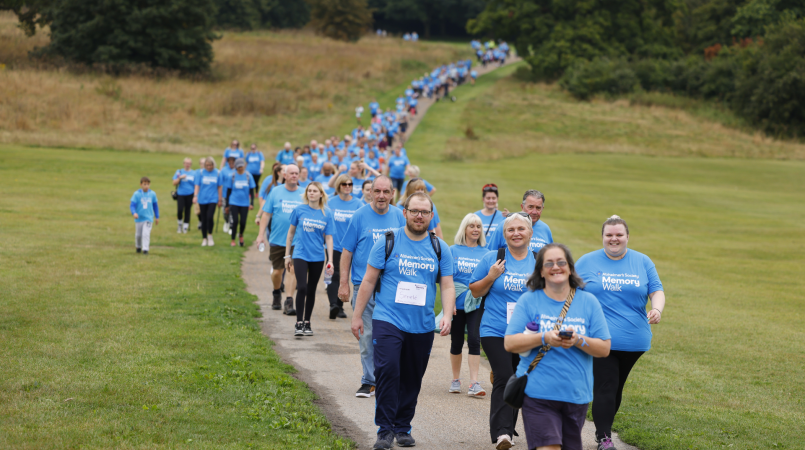 Crowd of people in blue Memory Walk t-shirts, walking in a line across a field, smiling.