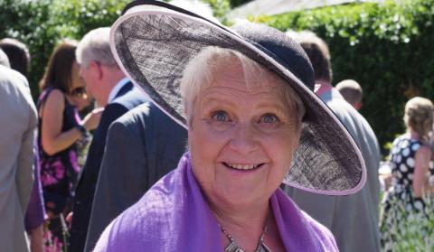 Di at a wedding wearing a large brimmed hat and a purple pashmina