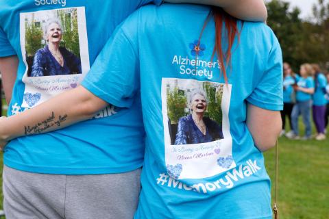 2 people arm in arm with their backs to the camera, wearing blue Memory Walk t-shirts with images of a loved one on the back.