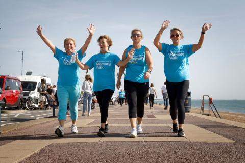 4 people in blue Memory Walk t-shirt, walking along the seafront with their arms in the air