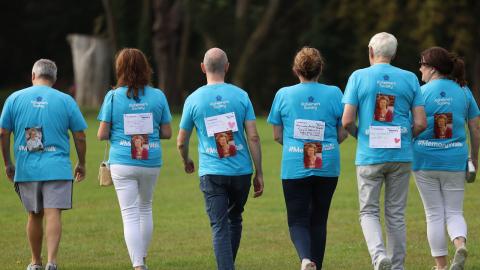 6 people in blue Memory Walk t-shirts, walking away from the camera with a picture of a loved one on their backs.