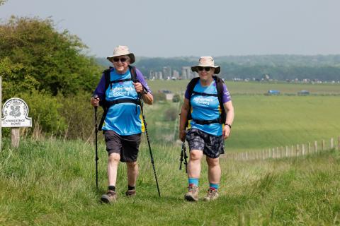 Two people trekking up hill in front of Stonehenge monument