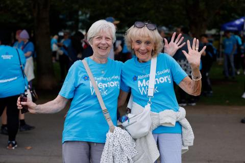 Two women in blue t-shits smiling and waving 