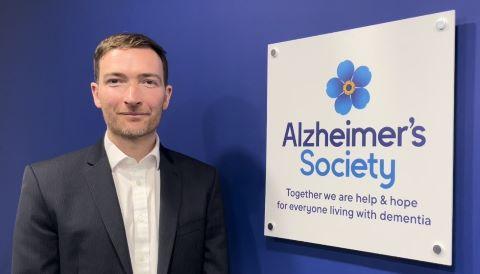 A suited man before to a wall with an Alzheimer's Society plaque 