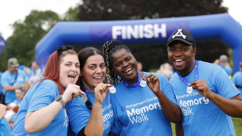 4 people wearing blue Memory Walk t-shirts, holding up their medals, smiling in front of the finish line.