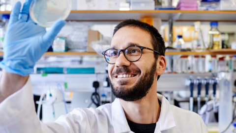 A man in a research laboratory holds up a petri dish